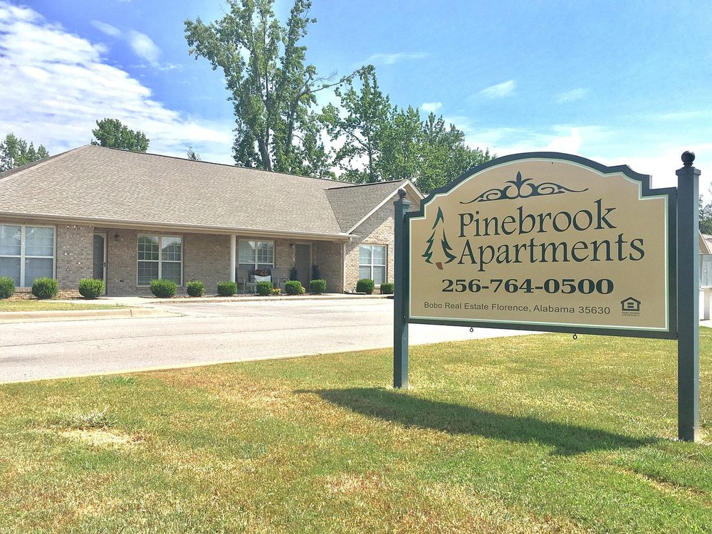 Pinebrook Apartments entrance sign with community behind it